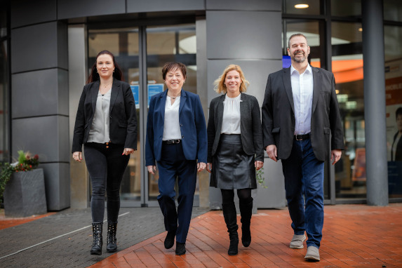 Berater und Beraterinnen der Firma ImmoKonzepte GmbH stehen vor einem grauen Gebäude und lächeln freundlich